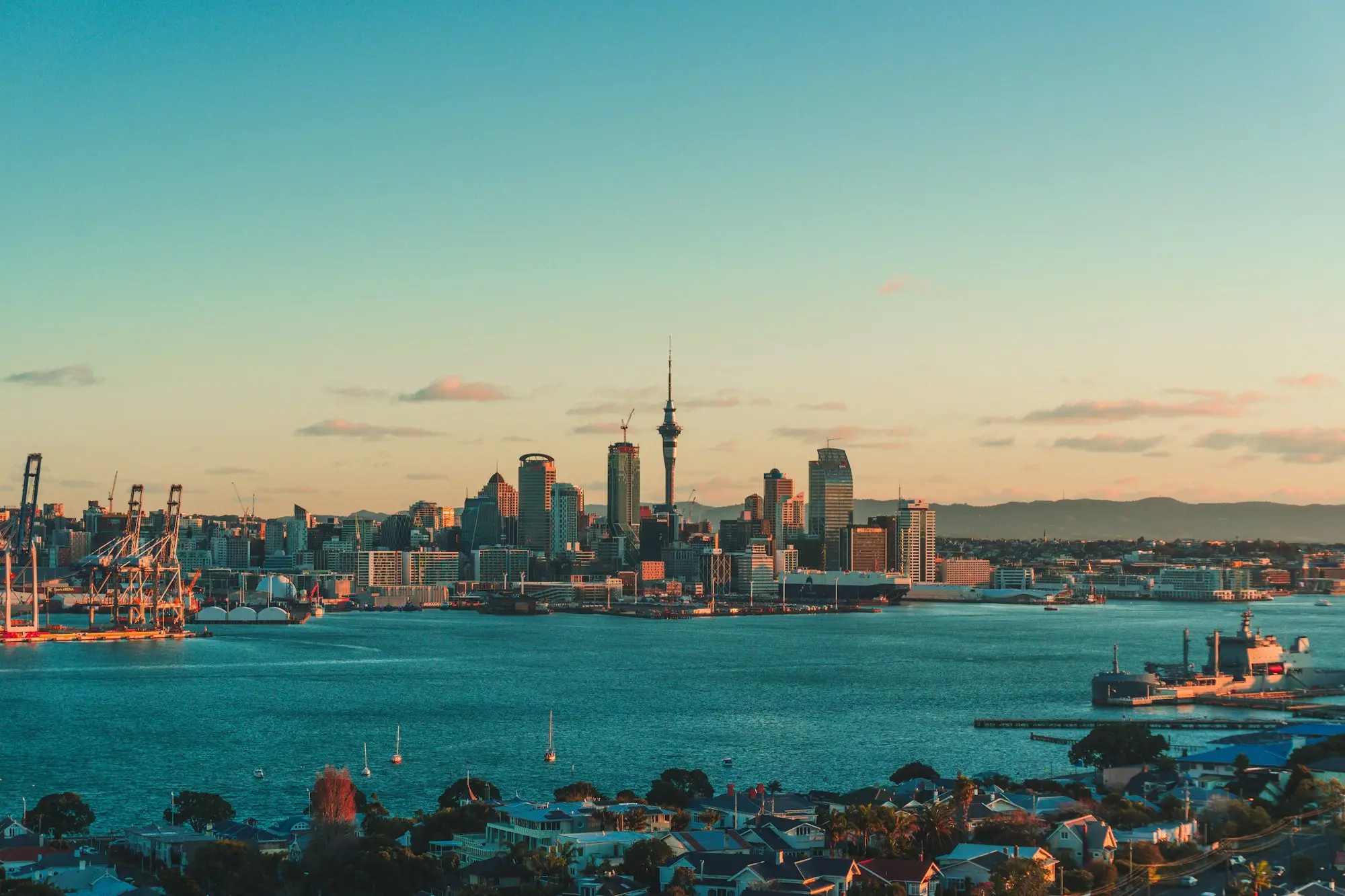 Auckland CBD skyline and Sky Tower across the Waitematā Harbour at dusk, ferries on the water