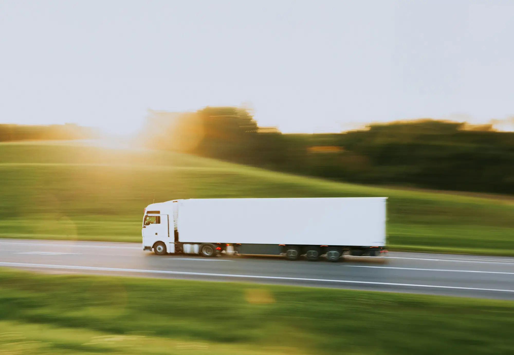 Refrigerated truck and trailer travelling along a rural highway past green paddocks at sunset, the kilometres it covers already paid for in road user charges